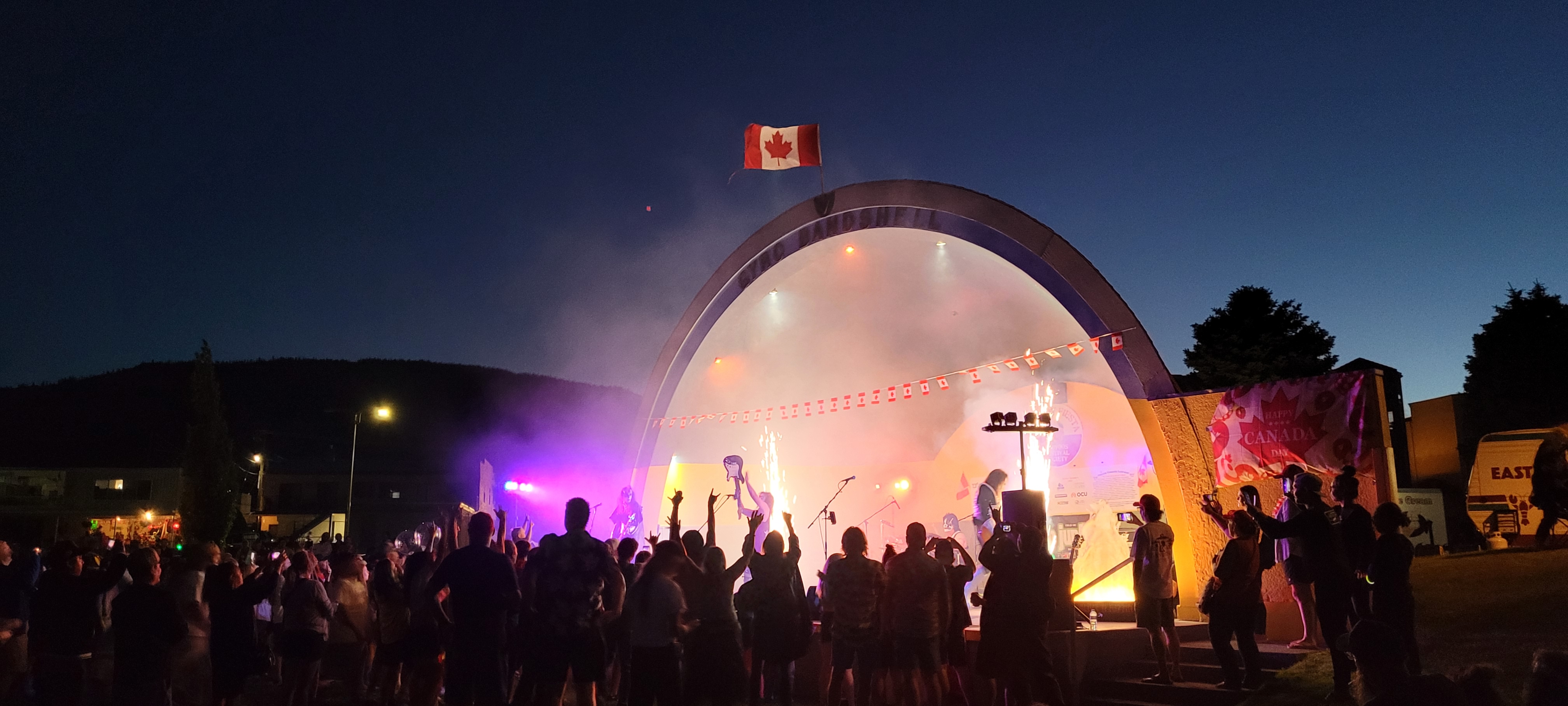 Massive crowd watching a live concert production at the outdoor bandshell under fireworks